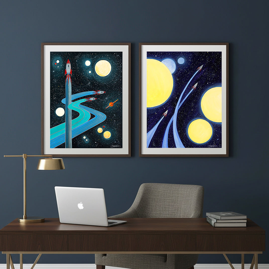 Two framed space themed limited edition art prints by Denise Marta-Burch,"Making Wakes" and "Between Worlds", are hanging in a home office.